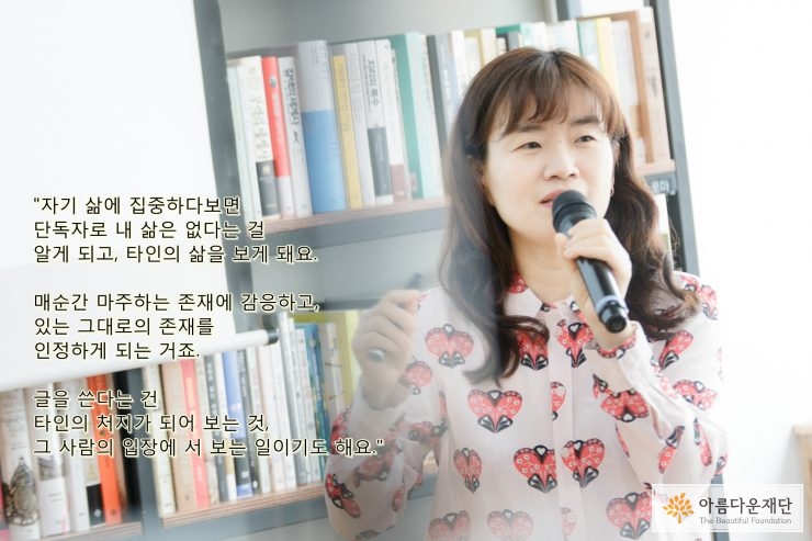 은유 작가가 마이크를 들고 강연을 하는 모습으로 뒤에는 책장 배경과 사진 왼쪽 배경에 강연 내용이 텍스트로 쓰여 있다