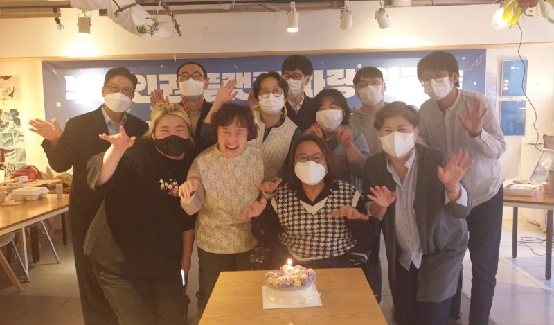 조직설립 1차 워크숍을 진행한 후 참가자들이 케잌을 앞에두고 활짝 웃으며 양 손을 올려 포즈를 취하고 사진을 찍고 있다.