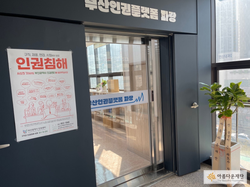파랑의 사무실 현관으로 어두운 계열의 색상으로 출입문 주변에 페인팅이 되어있고, 중앙 상단에는 희고 큰 글씨로 부산인권플랫폼 파랑이라고 적혀있다. 출입문 왼쪽에는 인권침해 신고 안내 포스터가 붙여져 있고 오른쪽에는 아름다운재단이 파랑에게 보낸 고무나무 화분이 놓여있다. 화분에는 '잔 물결이 큰 파도가 됩니다'라는 문구가 붙어있다. 현관문은 유리 자동출입문으로 장애인출입을 고려하여 턱이 없다.