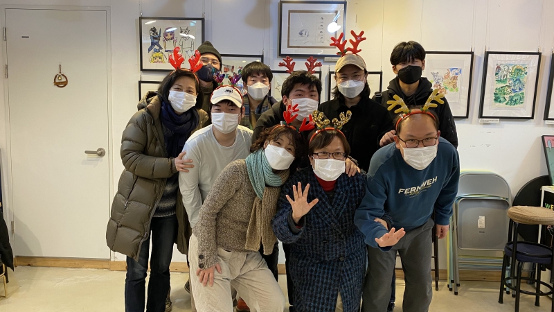 벽에 그림이 잔뜩 그려져 있고 앞에는 사부작 활동가들과 청년들이 사슴뿔 모양의 머리띠를 쓰고 사진을 찍고 있다.