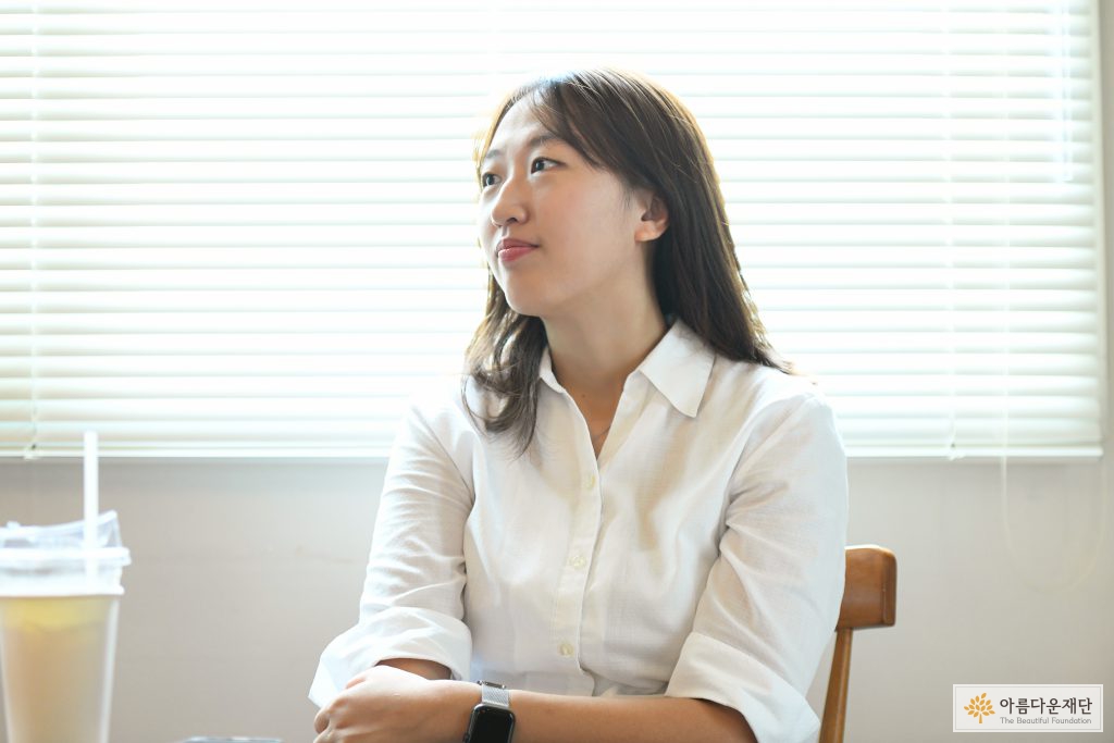 주지은활동가가 오른쪽 위쪽을 향해 보며 옅은 미소를 보이고 있다. 