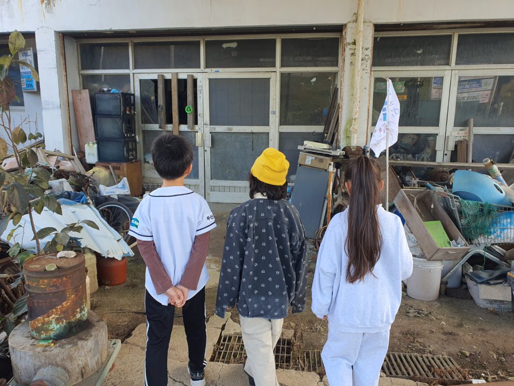 어른이 세 명이 낡은 건물 앞에 서 있는 뒷 모습.