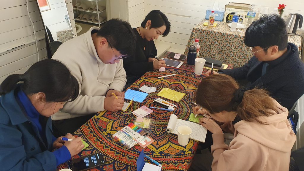 5명의 사람들이 메모지에 무언가를 적고 있다.