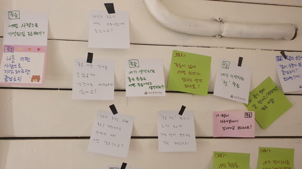 손글씨로 적은 포스트잇이 벽면에 가득 붙여 있다. 내가 생각하는 좋은 죽음은 어떤 죽음이라고 생각하는가? 죽음이 삶에 어떤 의미가 있다고 생각되나요? 등의 질문이 적혀 있다.