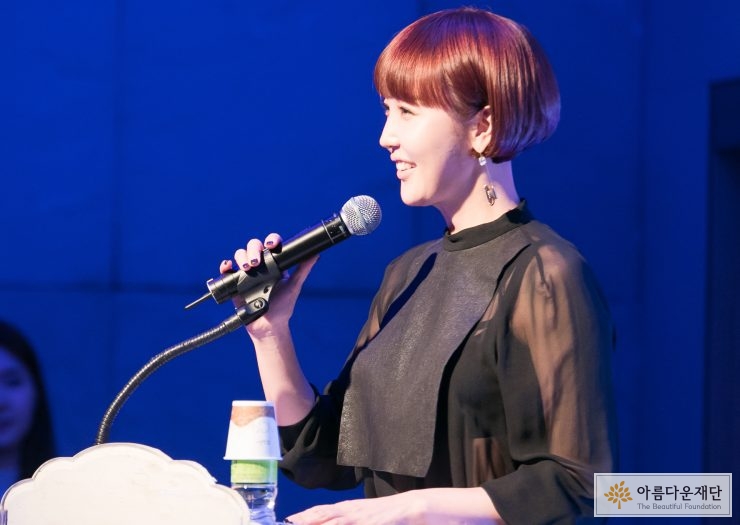검정색 옷을 입은 최은경 아나운서가 마이크로 말을 하고 있는 옆모습입니다.