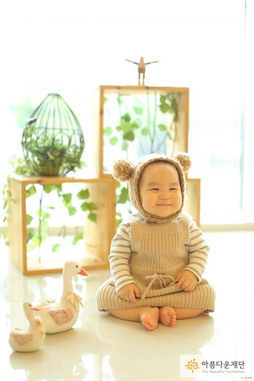 곰돌이 모자를 쓰고 앉아있는 아이 