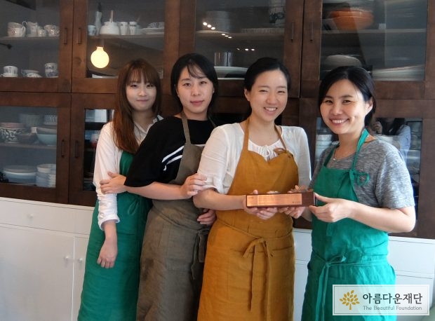 앞치마를 두른 여성 4명이 카메라를 보며 기념사진을 찍고 있음