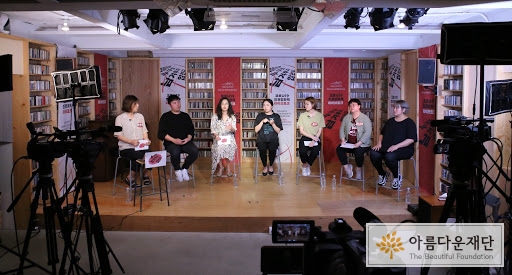 [사진2. 무대 위에서 코로나19 인권영화제: 누구도 남겨두지 않는다 라이브토크 1부가 진행되고 있다. 왼쪽부터 박한희 활동가, 김보석 수어통역사(한국농인LGBT), 랑희 활동가, 백수진 수어통역사, 희우 활동가, 진희 활동가, 남진영 수어통역사가 앉아있다.]