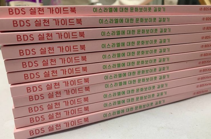 책자가 가득 쌓여 있다. 책등은 옅은 분홍색이며 제목은 ‘BDS 실천 가이드북: 이스라엘에 대한 문화보이콧 길찾기’이다