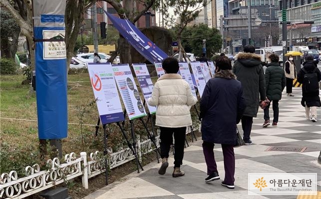 거리를 지나는 시민이 보드 전시를 살펴보고 있다