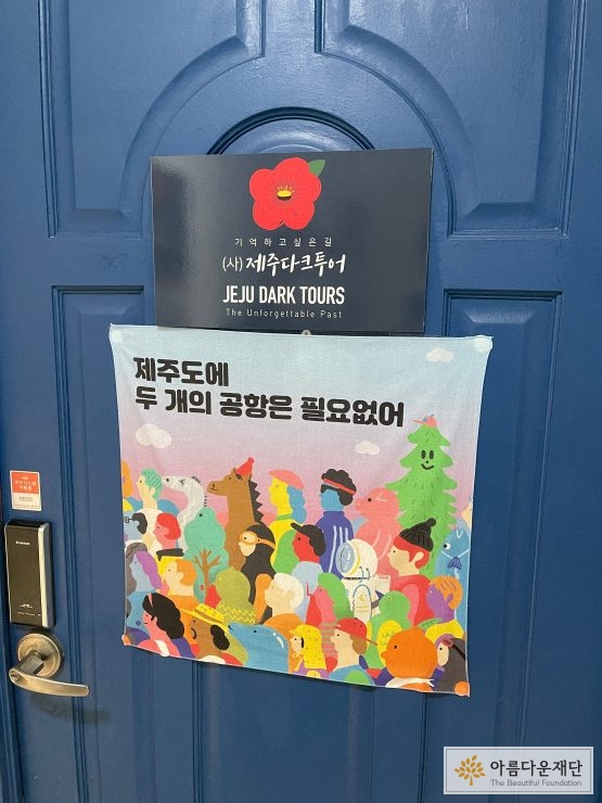제주다크투어 현관문에 붙어있는 현판과 천 포스터, 천 포스터에는 제주도에 두 개의 공항은 필요없어라고 쓰여있다.