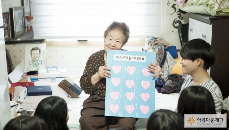 할머니가 장학생들에게 받은 편지를 들고 웃고 있다 