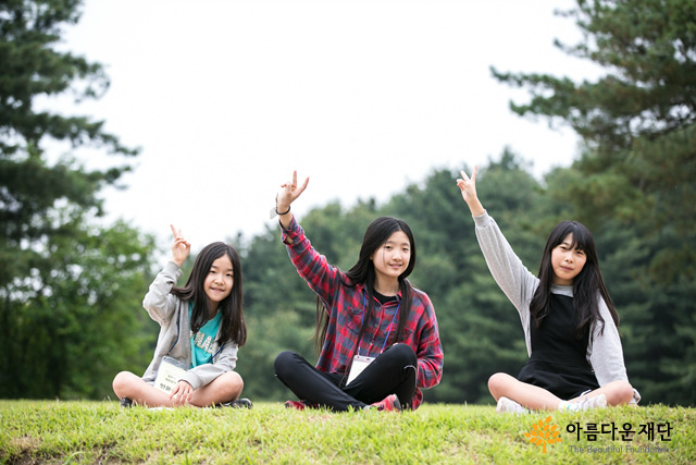 세명의 소녀들이 브이하는 손을 들고 웃고 있다