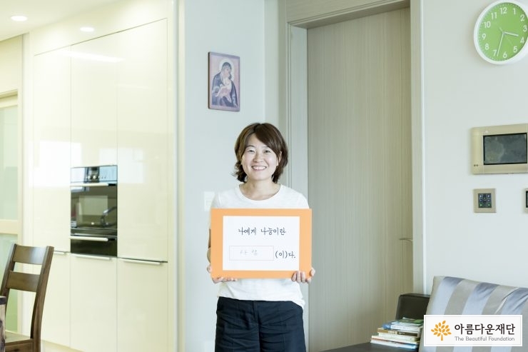 '나에게 나눔이란 사랑이다'라고 적힌 메모판을 들고 있는 기부자