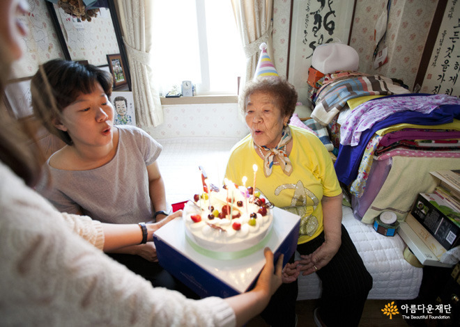귀여운 고깔모자를 쓰고 생일 케이크의 촛불을 불고 계시는 김군자 할머니